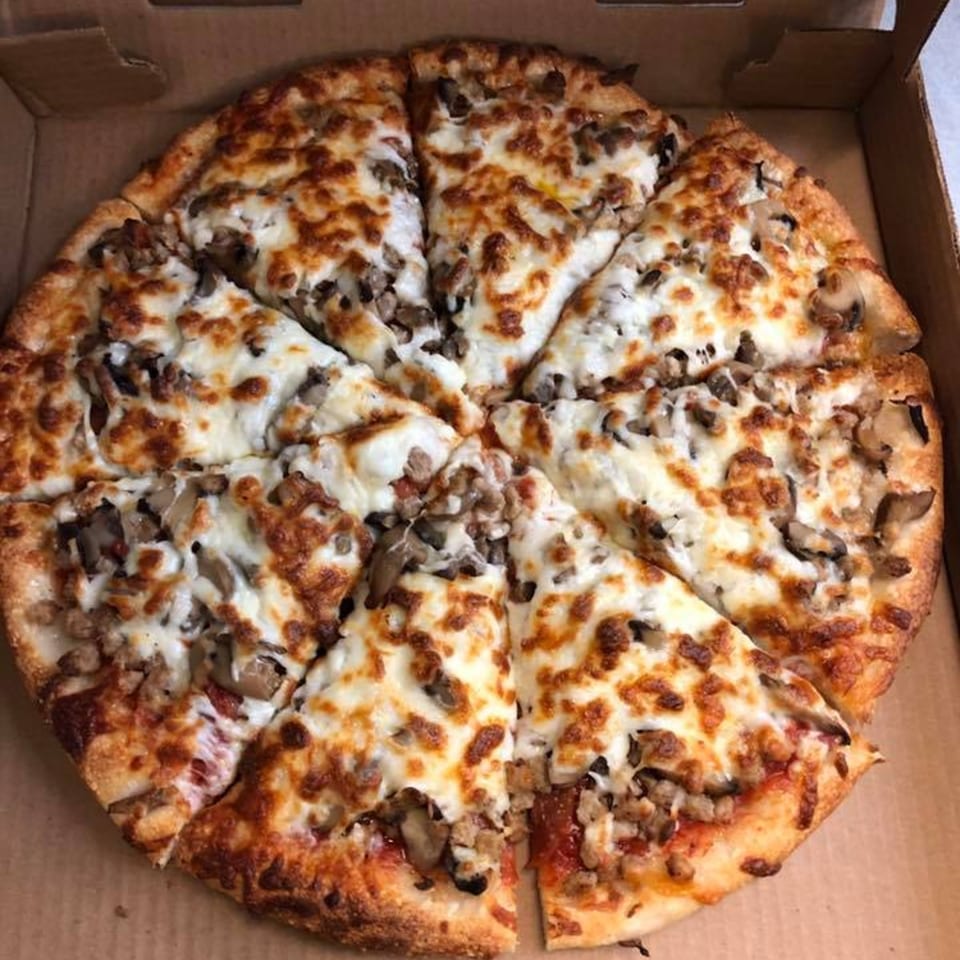 A whole Andy Boys Pizza with mushrooms and sausage, cut into slices, in a cardboard box.