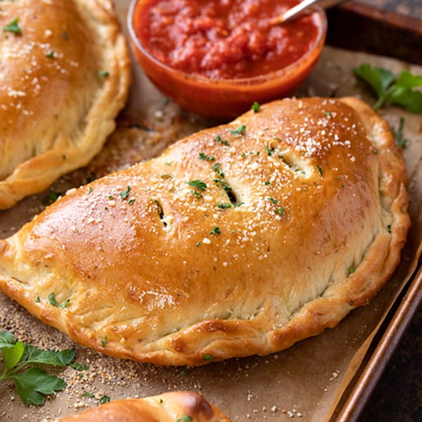 Golden-brown calzone sprinkled with parmesan and parsley, served with a side of red marinara sauce.