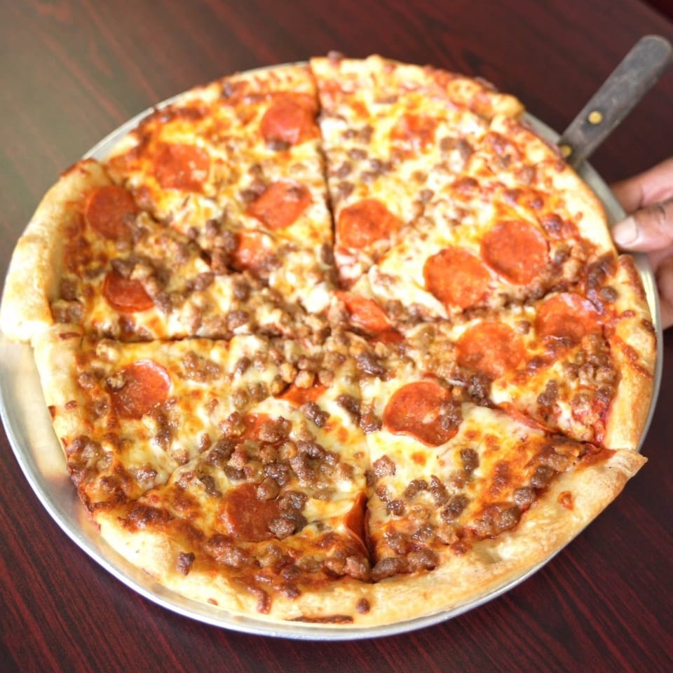 A freshly baked Andy Boys Pizza with pepperoni and sausage, served on a metal pan.
