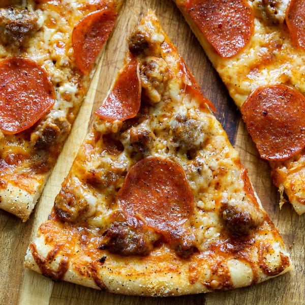 Three slices of Andy Boys pepperoni and sausage pizza on a wooden cutting board.