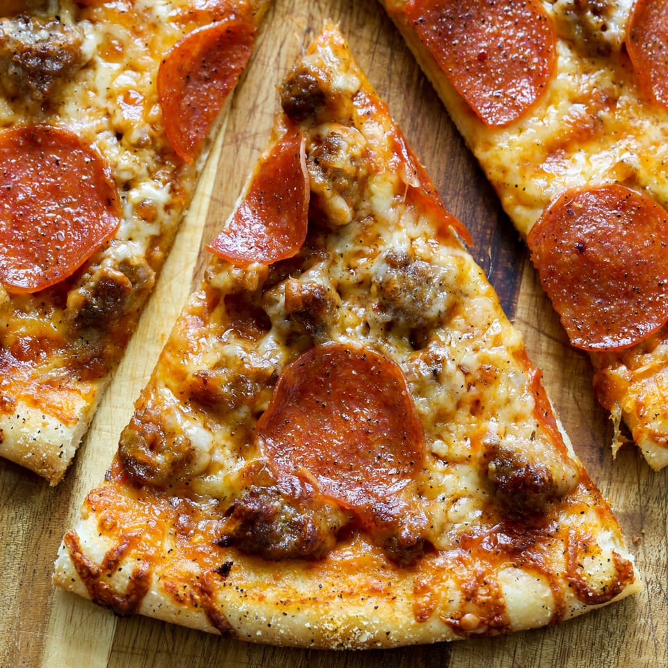 Three slices of Andy Boys pepperoni and sausage pizza on a wooden cutting board.